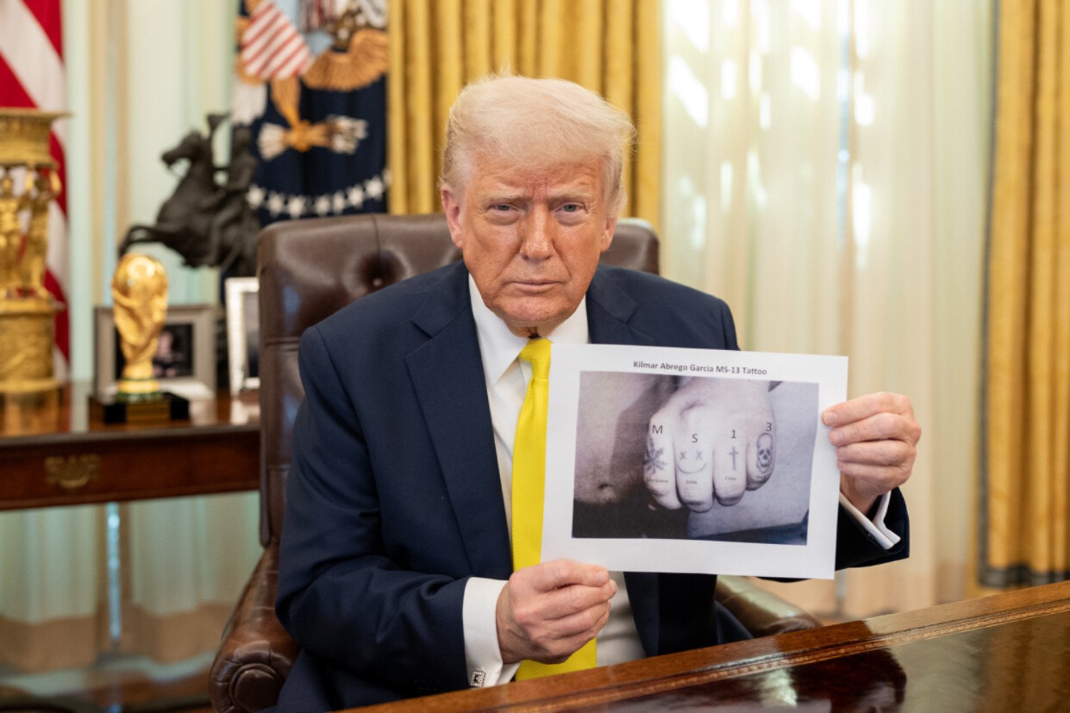 President Donald Trump holds up an image of a hand that's been photoshopped to add the characters "MS-13" at the White House on April 18, 2025.